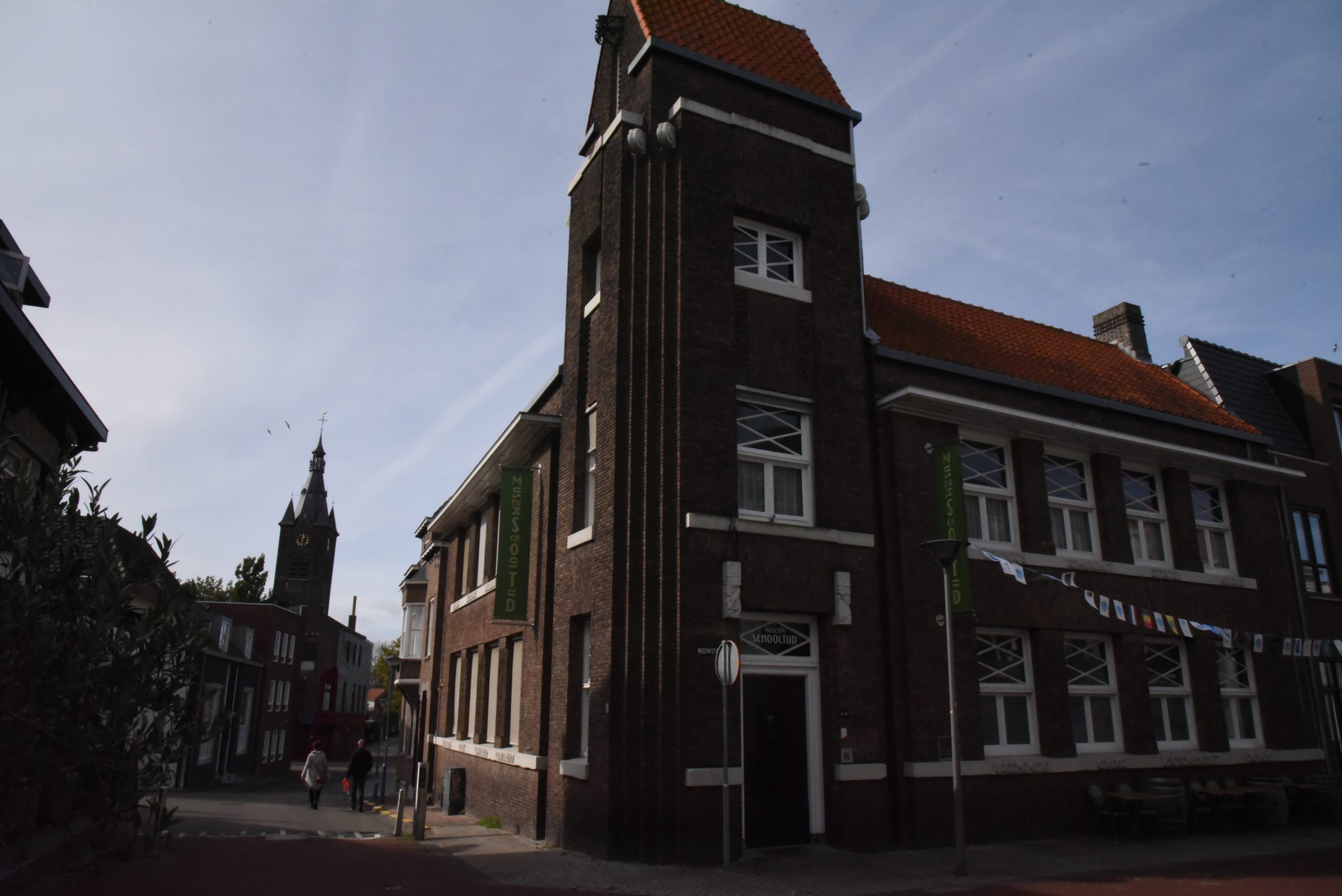 Ietwat donkere foto van een tweezijdig aangebouwd hoekpand uit omstreeks 1920 opgetrokken uit rode baksteen. Aan weerszijden van de torenachtige hoekpartij bevinden zich vier traveeën brede langsgevels.
