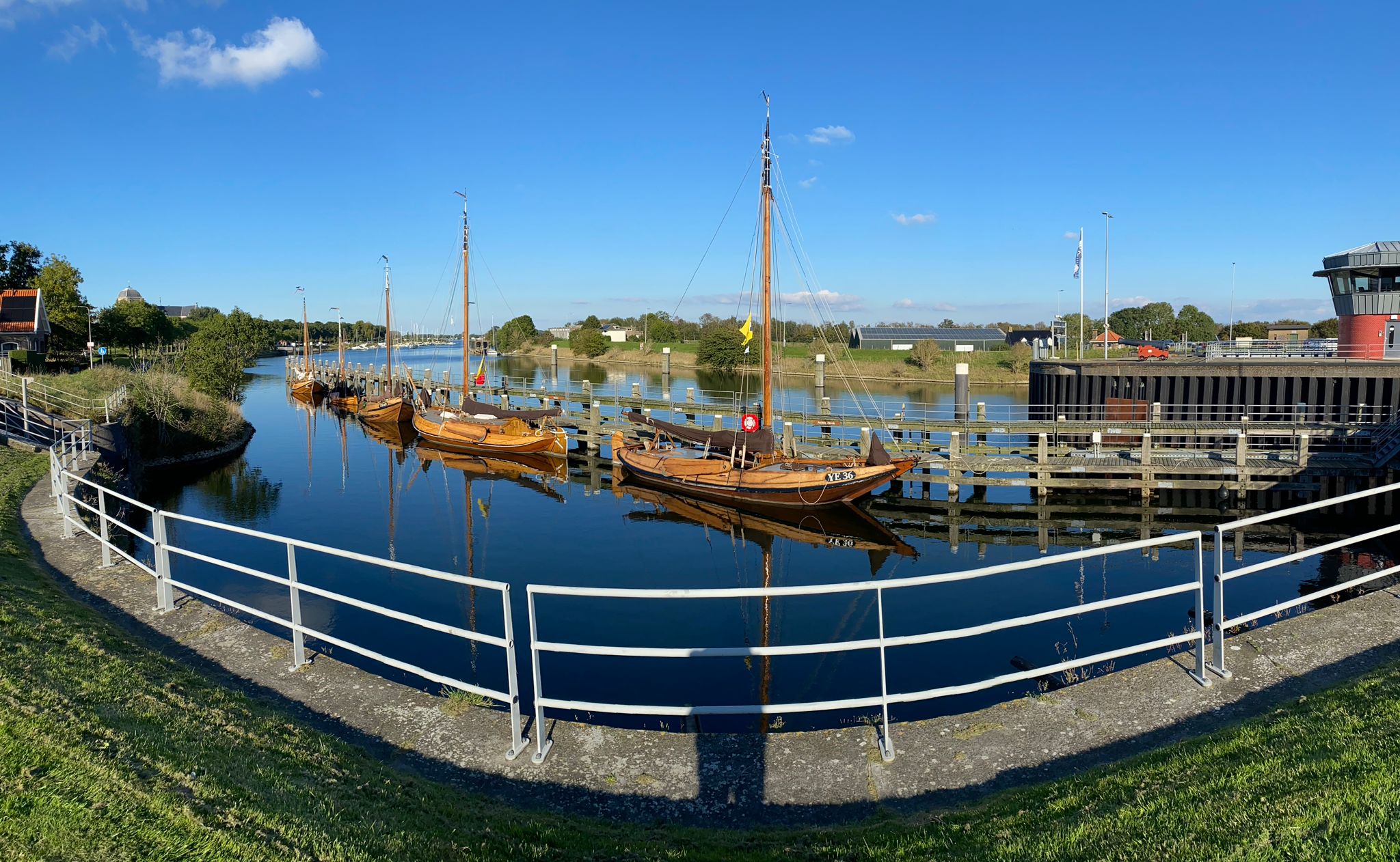 Panoramafoto van vijf houten hoogaarzen op een rij bij de stijger bij de sluizen van Veere. Het is een mooie, windstille dag (de vlaggen hangen er slapjes bij).