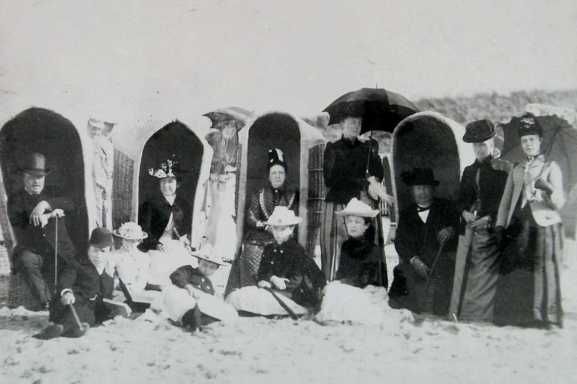 Een groep mensen zit en staat rondom vier strandstoelen op het strand in Domburg rond 1900.