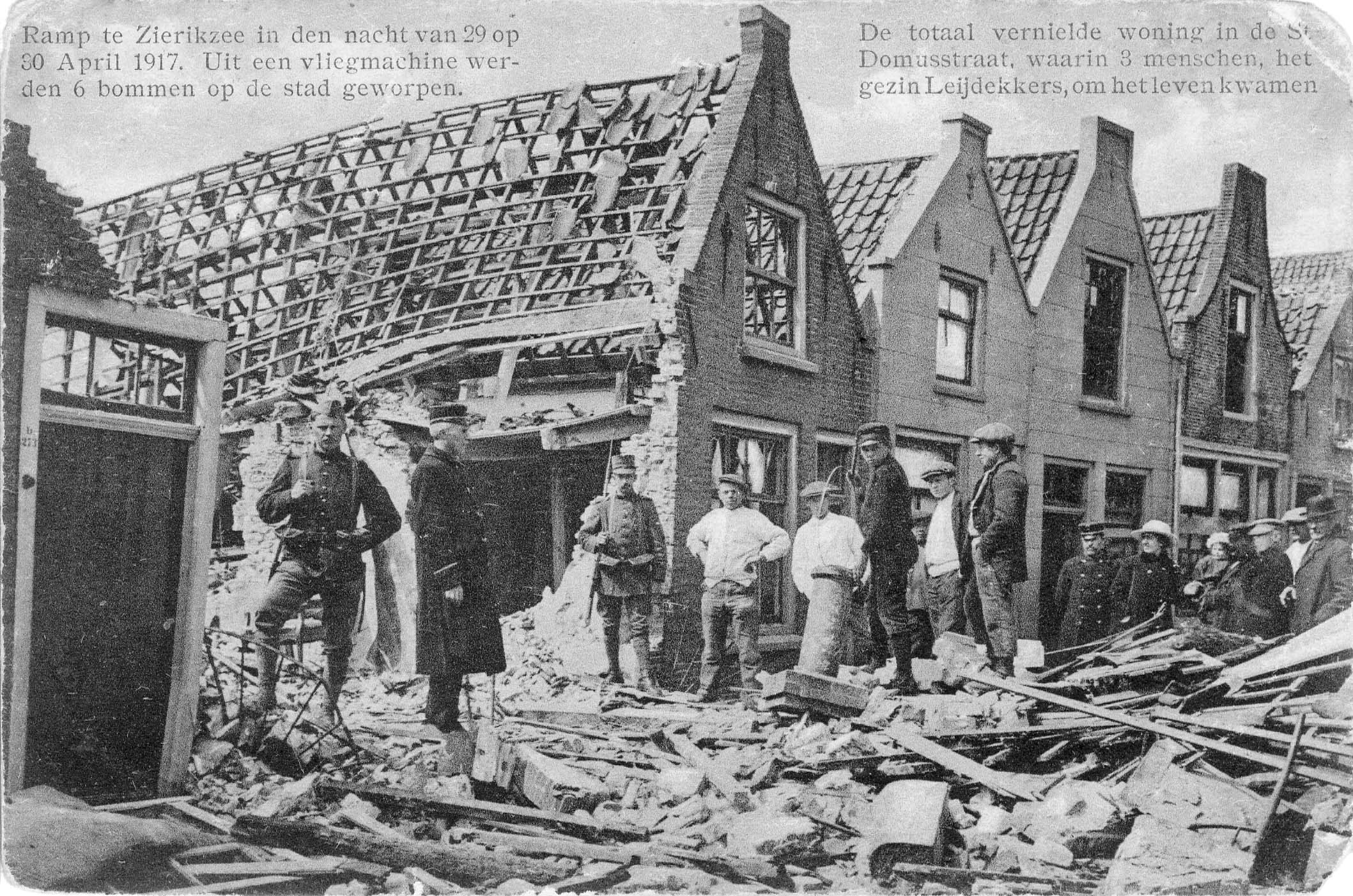 Een ansichtkaart van een in puin gelegde straat. Links bovenin staat de tekst: Ramp te Zierikzee in den nacht van 29 op 30 april 1917. Uit een vliegmachine werden 6 bommen op de stad geworpen. Rechts bovenin staat de tekst: De totaal vernielde woning in de St. Domusstraat, waarin 3 menschen, het gezin Leijdekkers, om het leven kwamen. Op de kaart is een gat te zien op de plek waar het huis van de familie Leijdekkers stond. Op de foto zijn meerdere beschadigde huizen te zien, waarvan alleen nog maar het geraamte staat. Op het puin voor de huizen staan meerdere mannen, sommigen in uniform van de politie of militaire dienst.