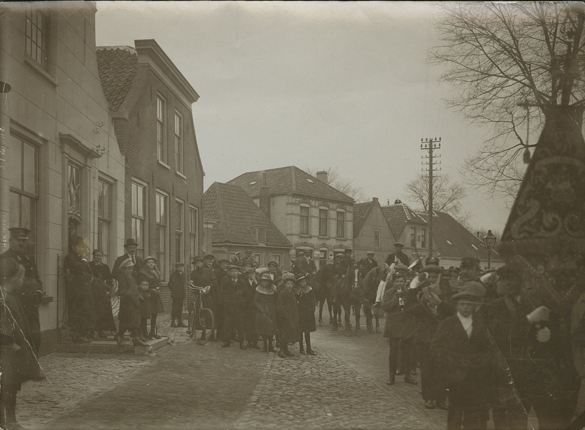 Een zwart-wit foto met op de voorgrond een harmonie en op de achtergrond mannen op paarden: de straô rijders.