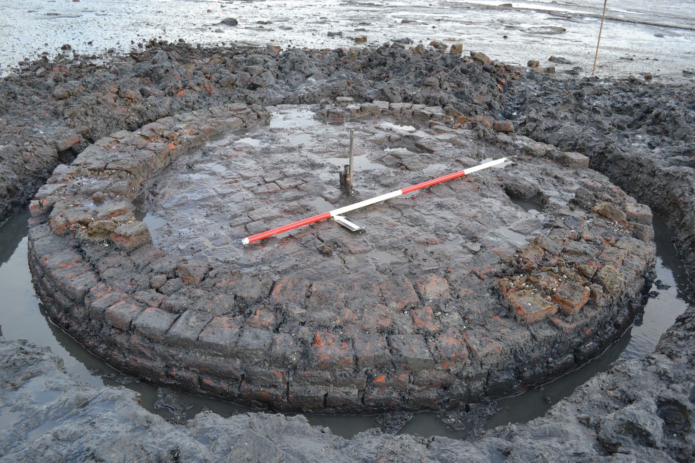 Een ronde cirkel gemaakt van bakstenen omringd door water en modder.